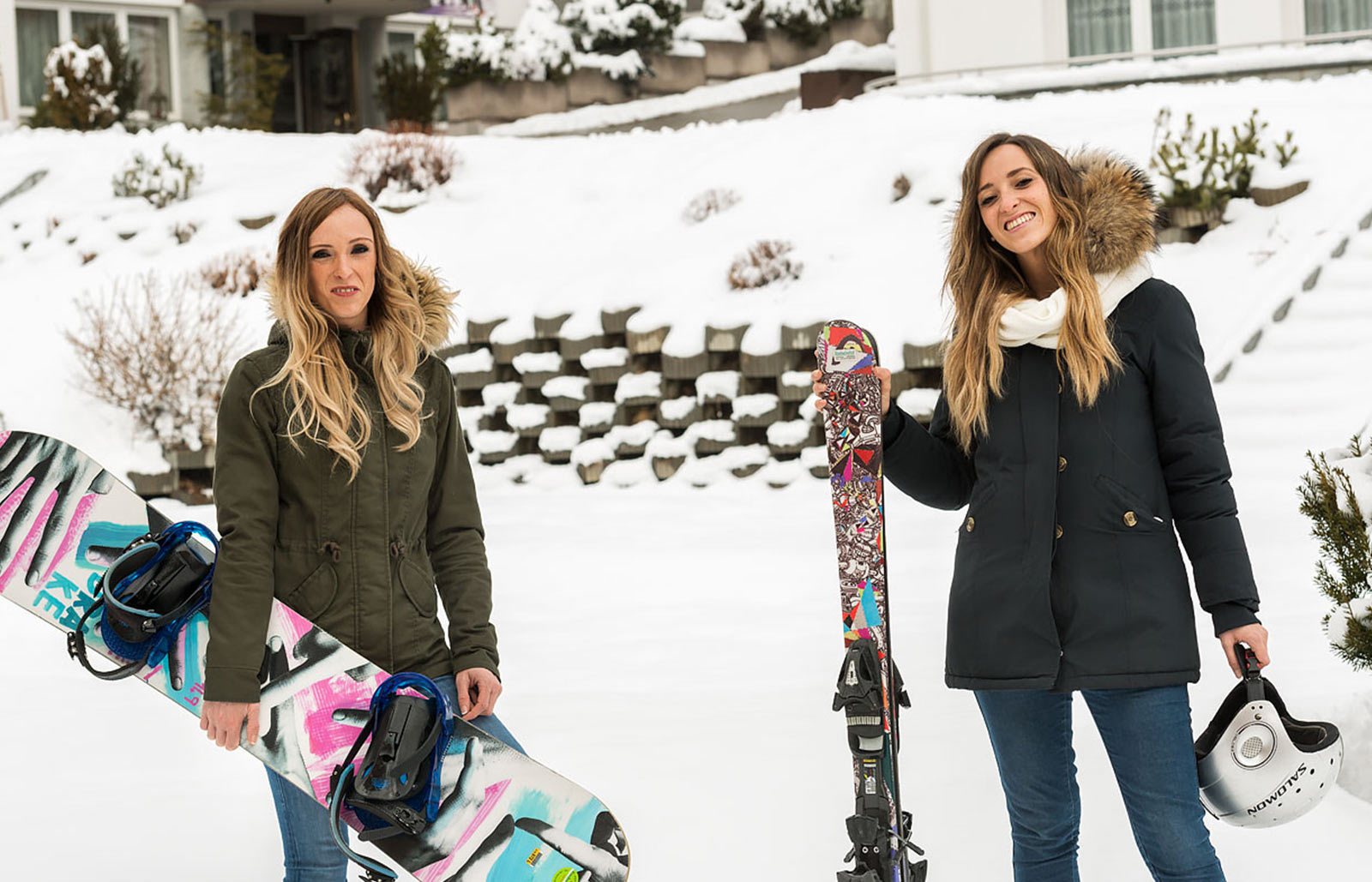 Zwei Damen mit geliehenem Snowboard und Skiern freuen sich über die Abfahrt