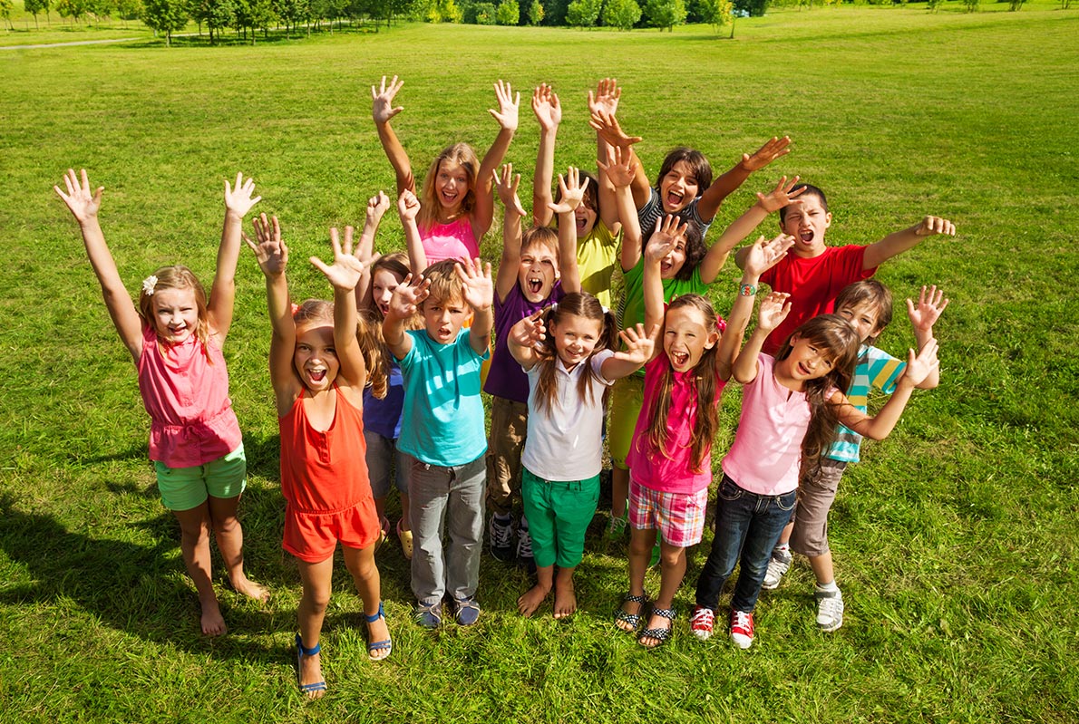 Eine Gruppe von Kindern die lachen auf einer Wiese an einem wolkenlosen Sommertag